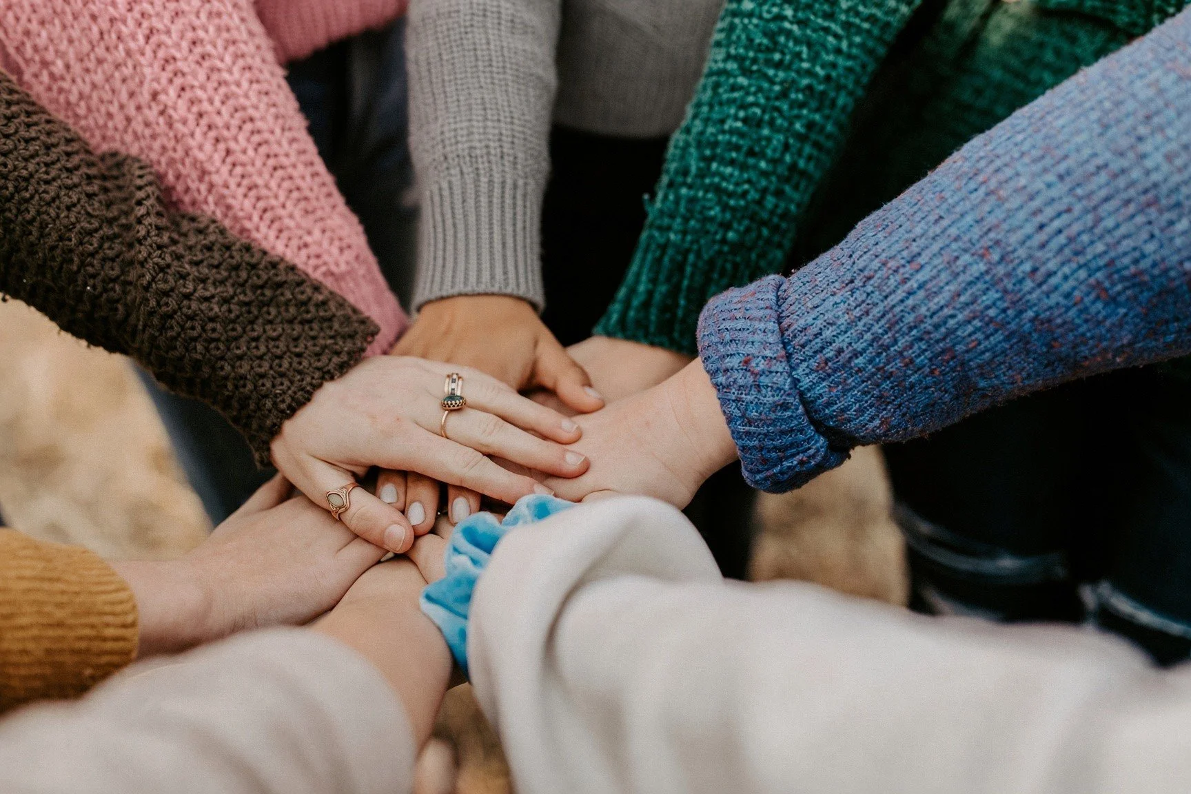A circle of hands stacked together at the centre of a group of women, in a gesture of unity and support.