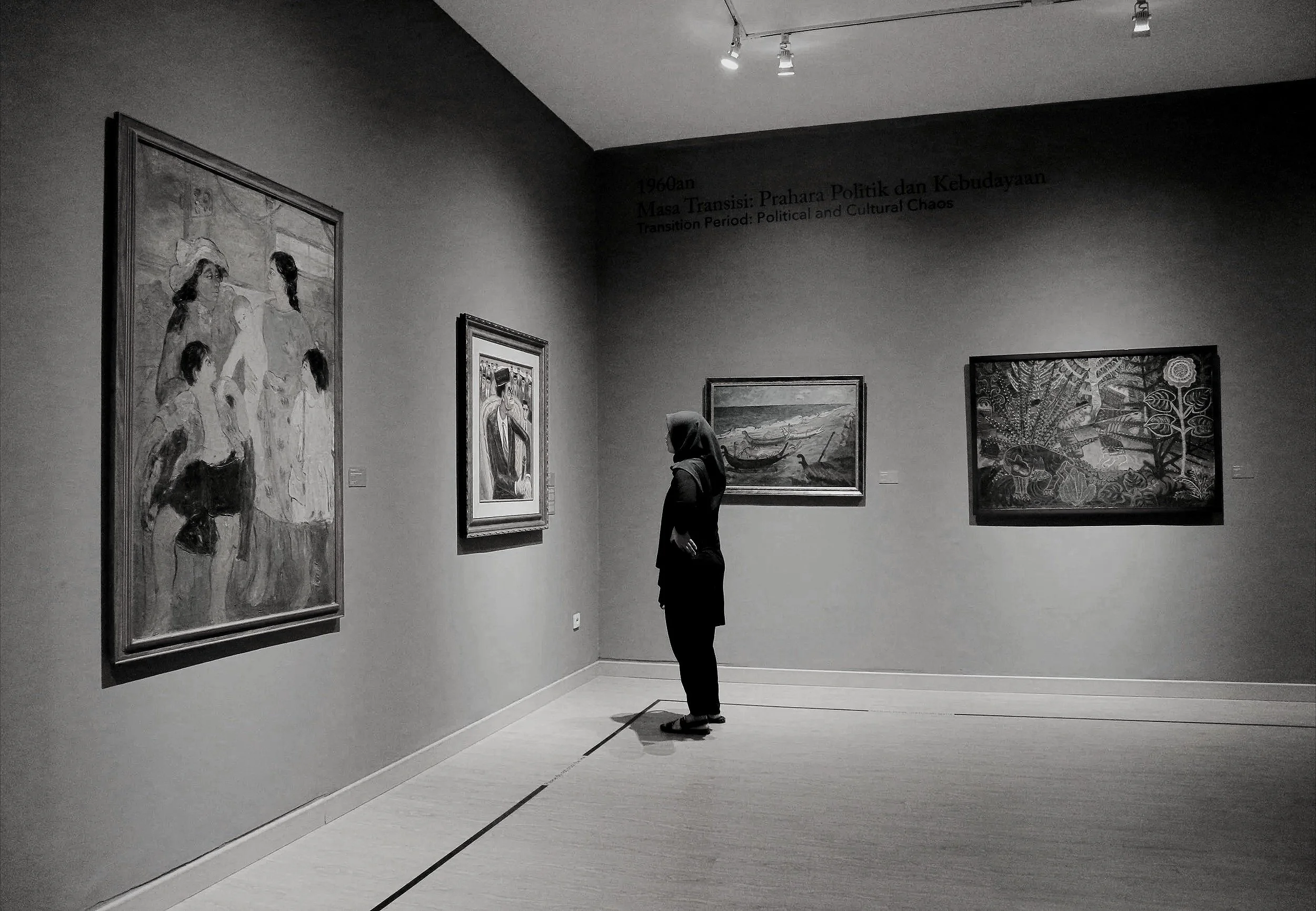 A woman in a hijab standing and viewing paintings in an art gallery.