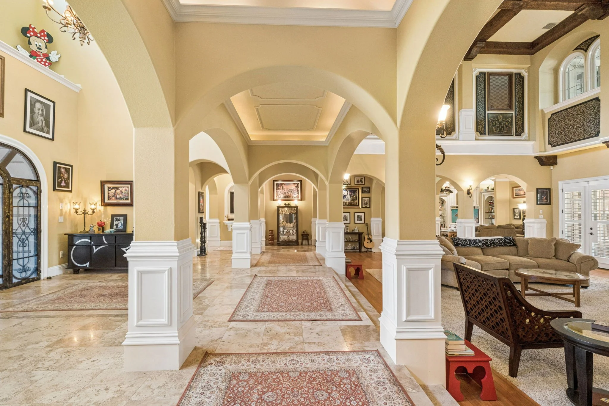 A spacious, elegant living room with high ceilings, arches, artwork, and a cozy seating area.