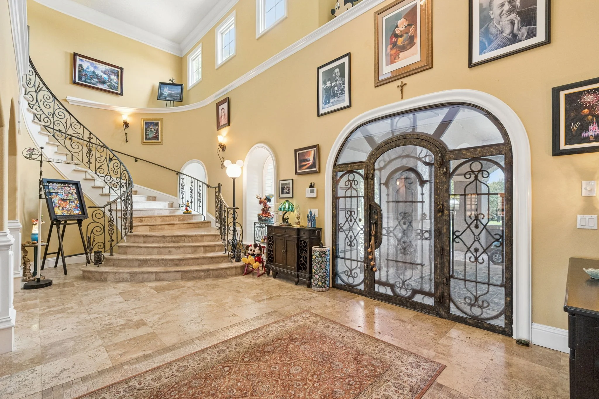 Entryway with staircase, framed pictures on yellow wall, decorative items, and double glass and wrought iron doors.