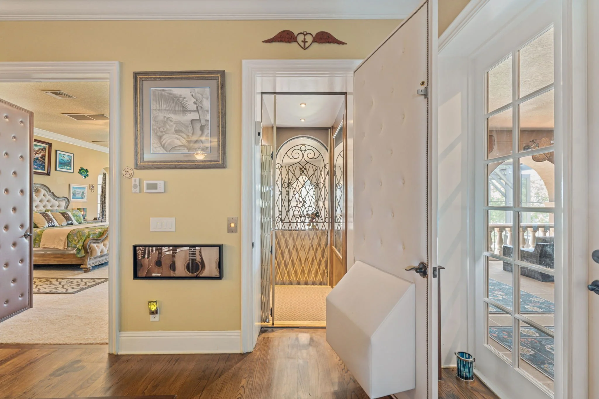 View from entrance of a home's interior showing a living room on the left and a hallway leading to another room on the right, with various artwork on the walls and natural light coming through the windows.