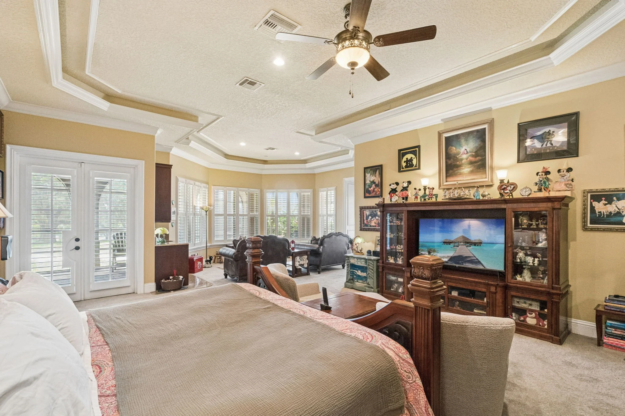 Living room with a beige sofa, wooden furniture, a flat-screen TV, artwork, and a row of collectible figurines on the fireplace mantel.