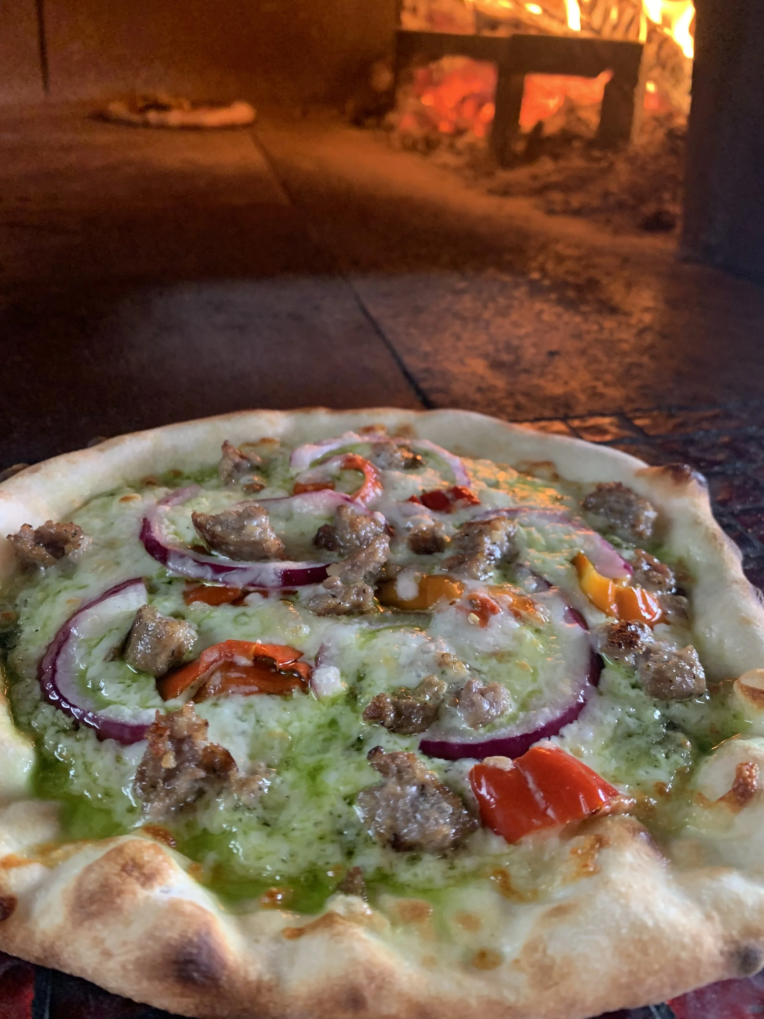 Close-up of a pizza with sausage, red onions, bell peppers, and green herbs, baked in a brick oven.