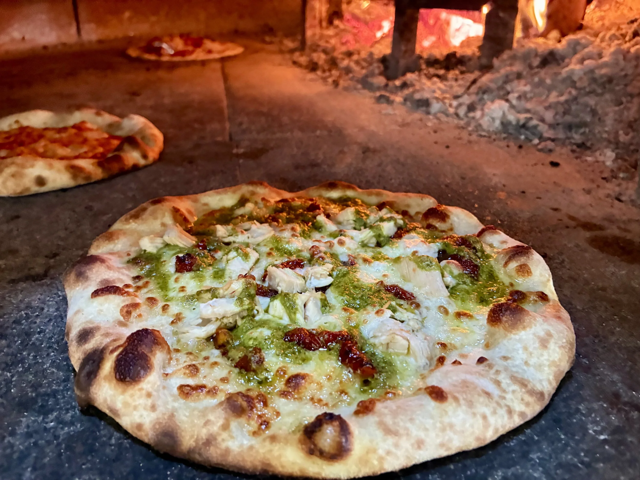 Pizza being baked in a wood-fired oven with visible flames and embers inside.