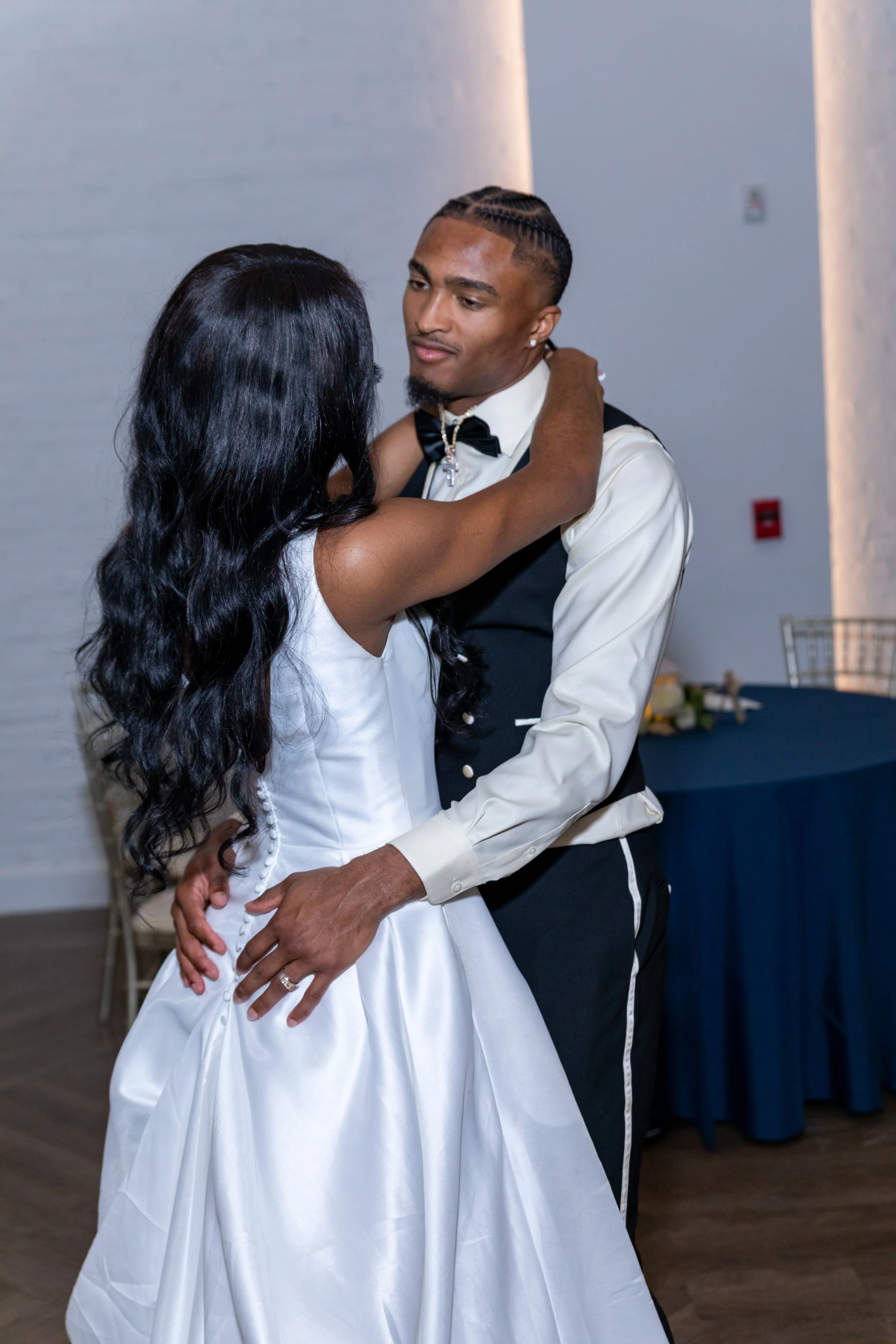 A couple dressed in formal wedding attire dancing closely at their wedding reception, with the bride in a white gown and the groom in a tuxedo.