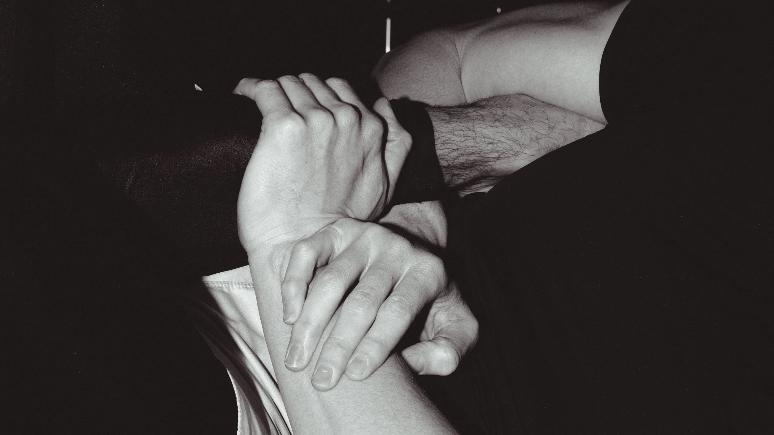Close-up of two hands holding each other, with one hand gently grasping the other, in black and white.