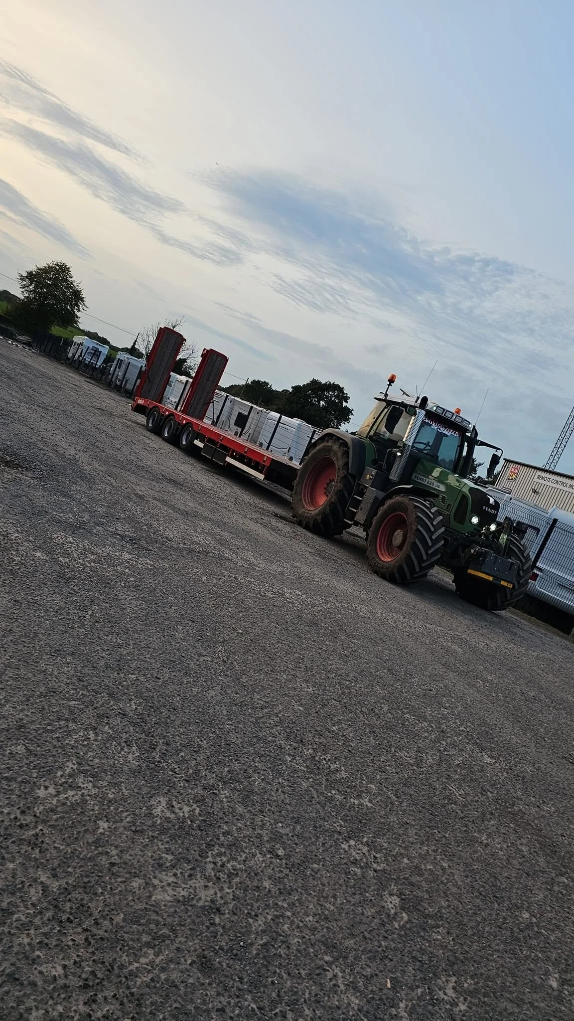 A large green tractor pulling a flatbed trailer with white storage containers in an outdoor lot.