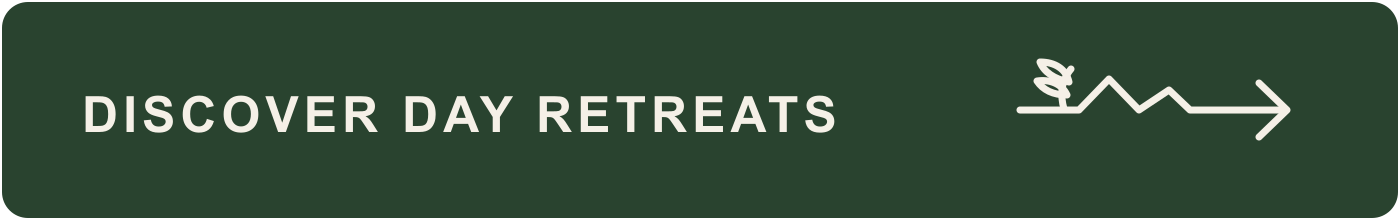 Green outdoor sign with white text reading "Discover Day Retreats" and a white arrow pointing to the right, with a mountain and tree icon.