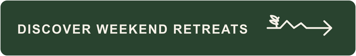 Green outdoor sign with white text that reads 'Discover Weekend Retreats' and an arrow with a small leaf and mountain illustration.