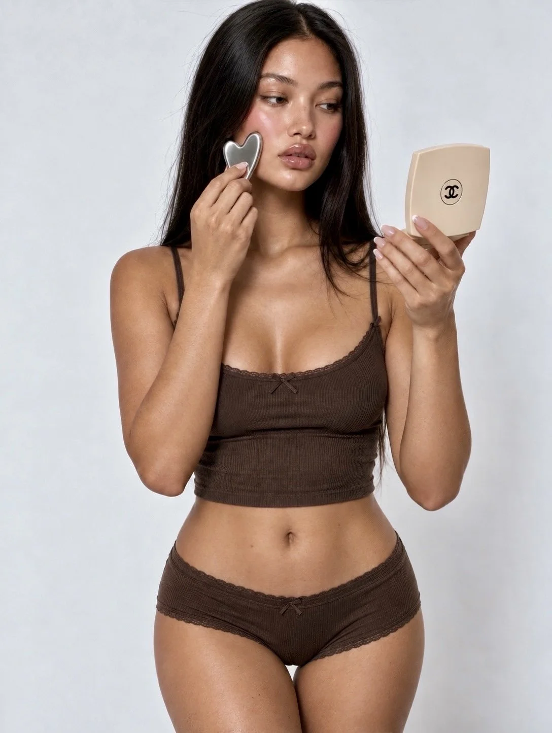 A woman in brown lace-trimmed underwear holding a compact mirror and a makeup brush to her cheek.