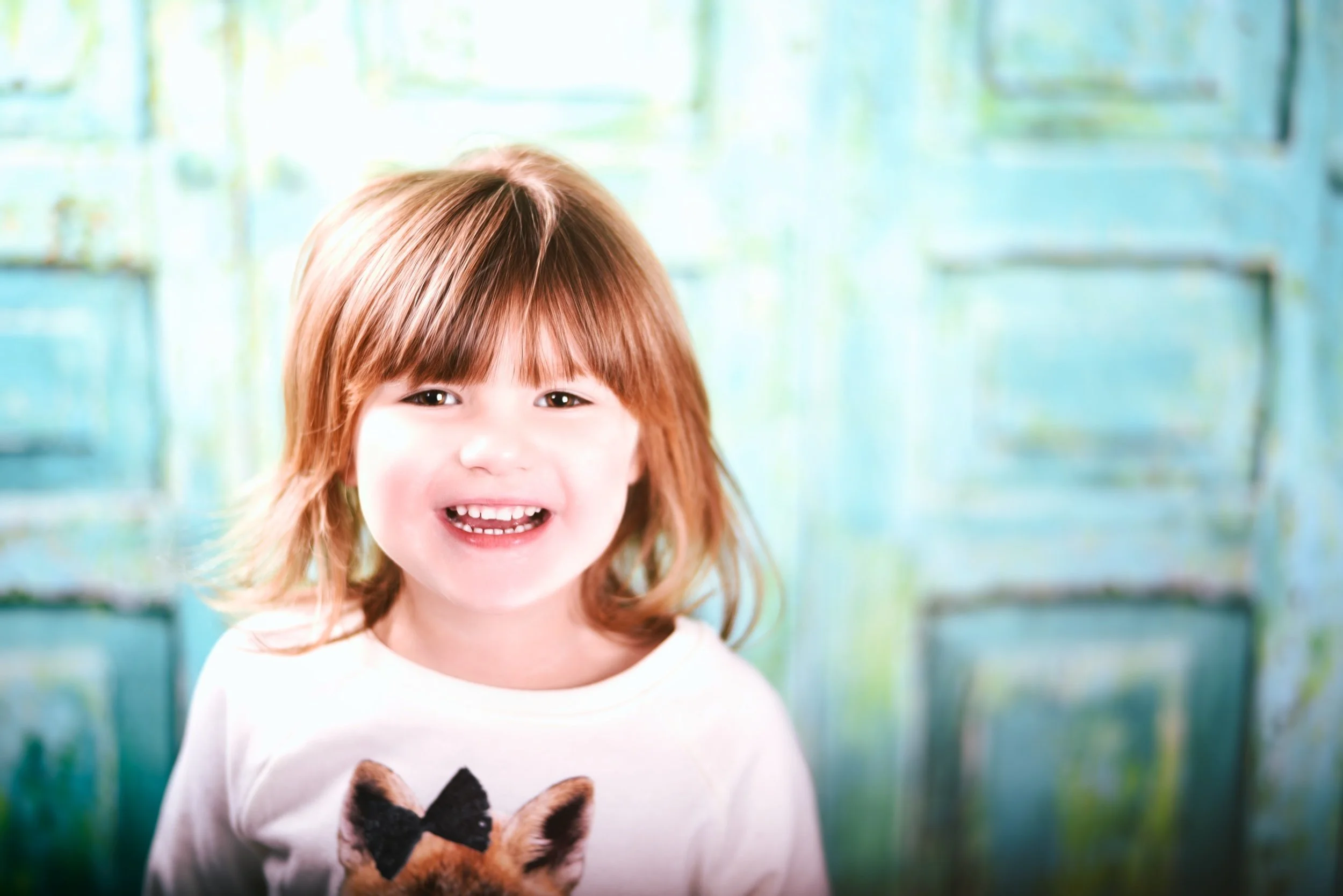 A young girl with red hair and a big smile holding a small dog with a bow tie.