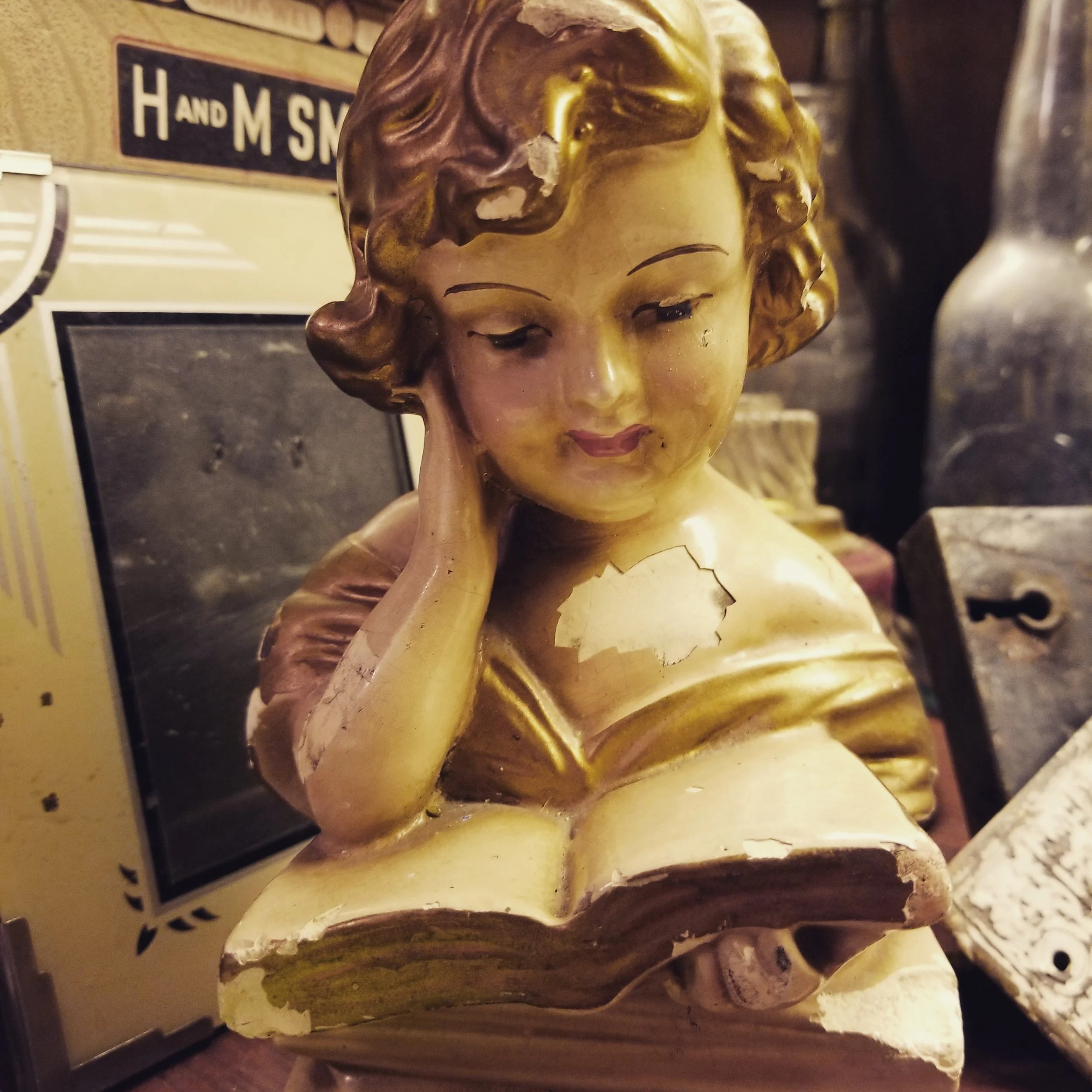 A close-up of a vintage-style bust of a woman reading a book sitting on a shelf.