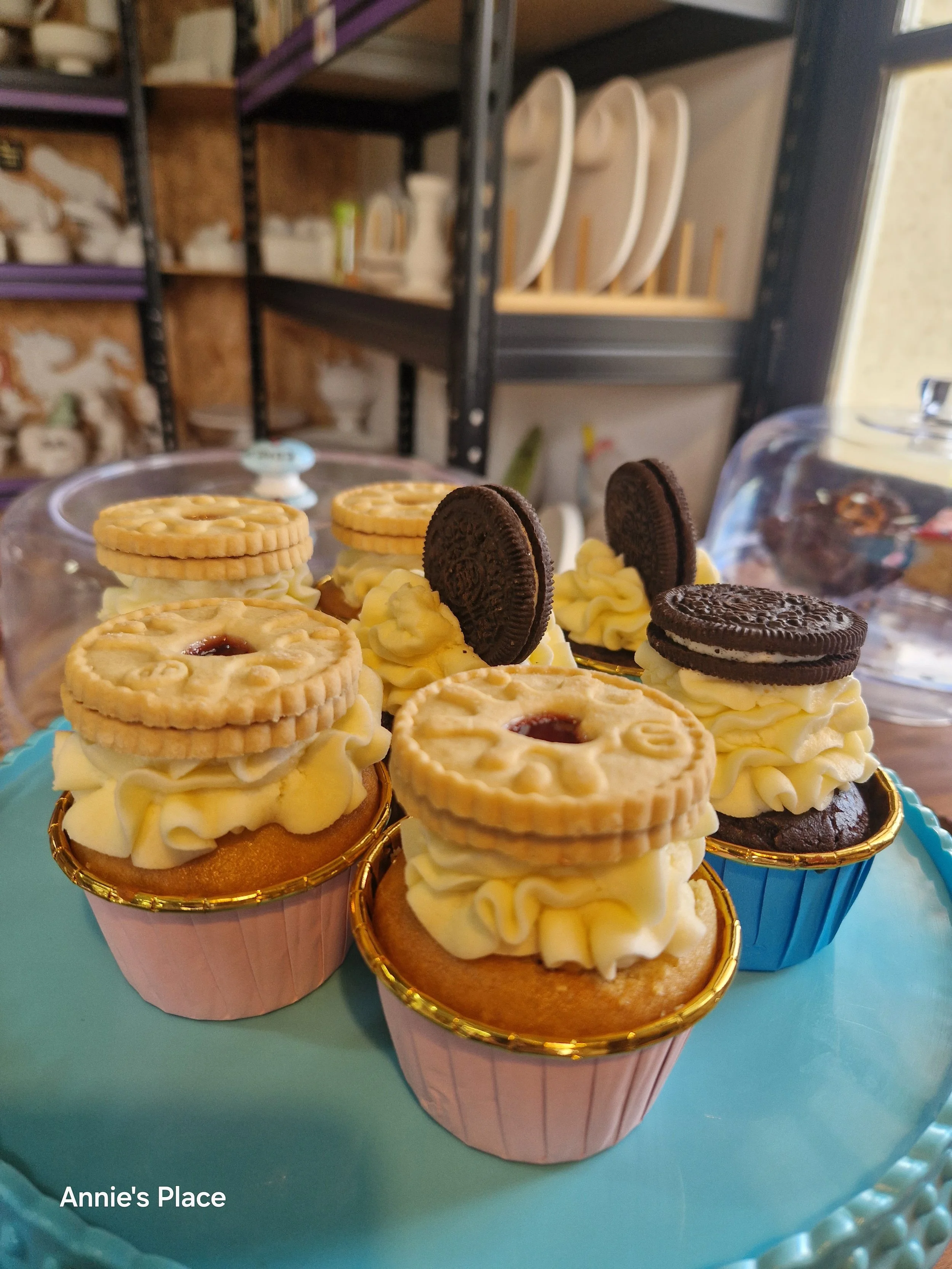 Cupcakes topped with cookies and Oreo cookies on blue and pink cupcake liners, displayed on a light blue table.