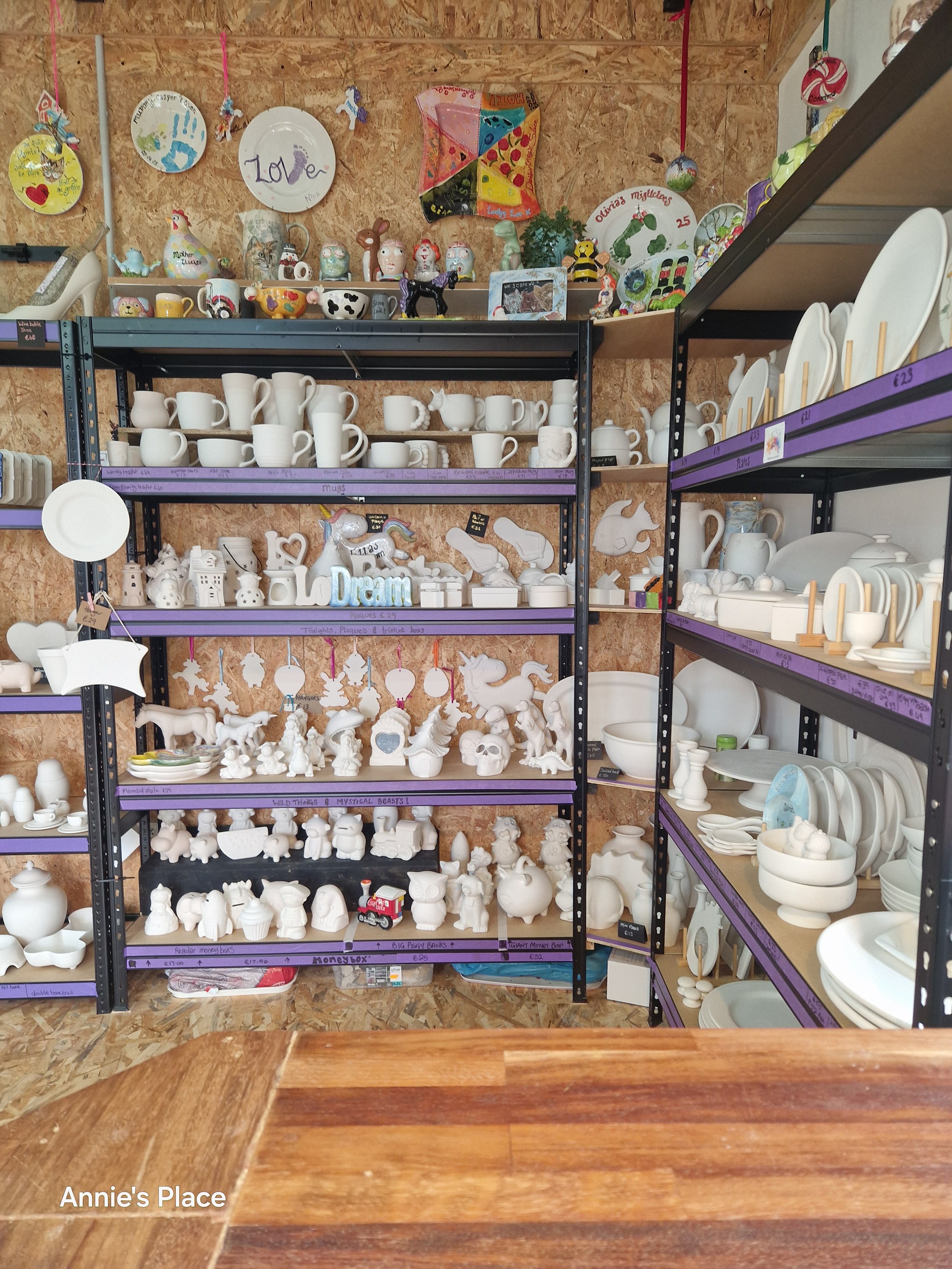 Shelves displaying unpainted ceramic figurines, mugs, plates, and ornaments at Annie's Place store.