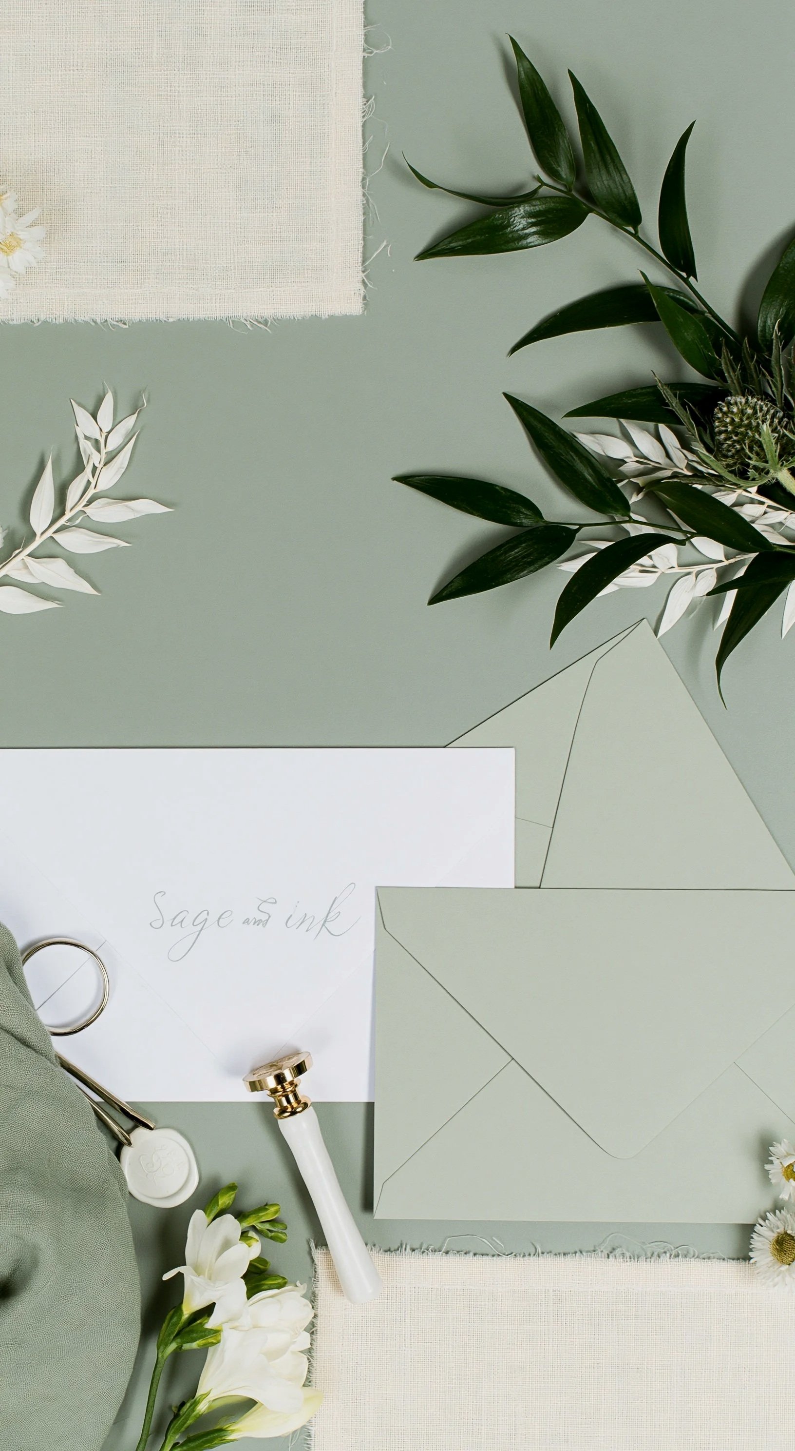 Flat lay of wedding or event stationery, foliage, and a ring on a fabric surface in muted, natural tones