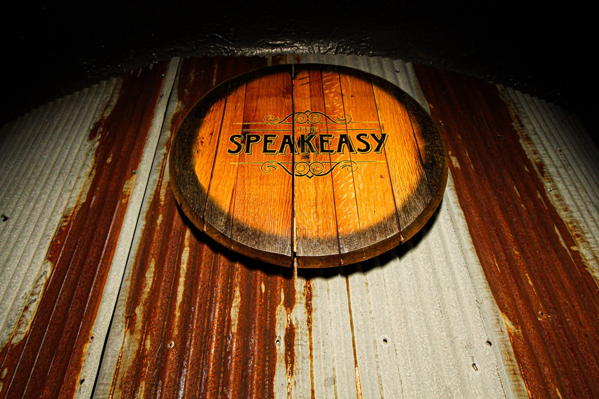 Wooden sign with the words 'The Speakeasy' hanging on a rusty corrugated metal wall.