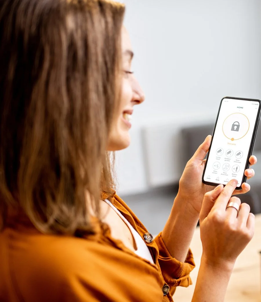 Person using a smartphone with a smart home security app displayed on the screen.