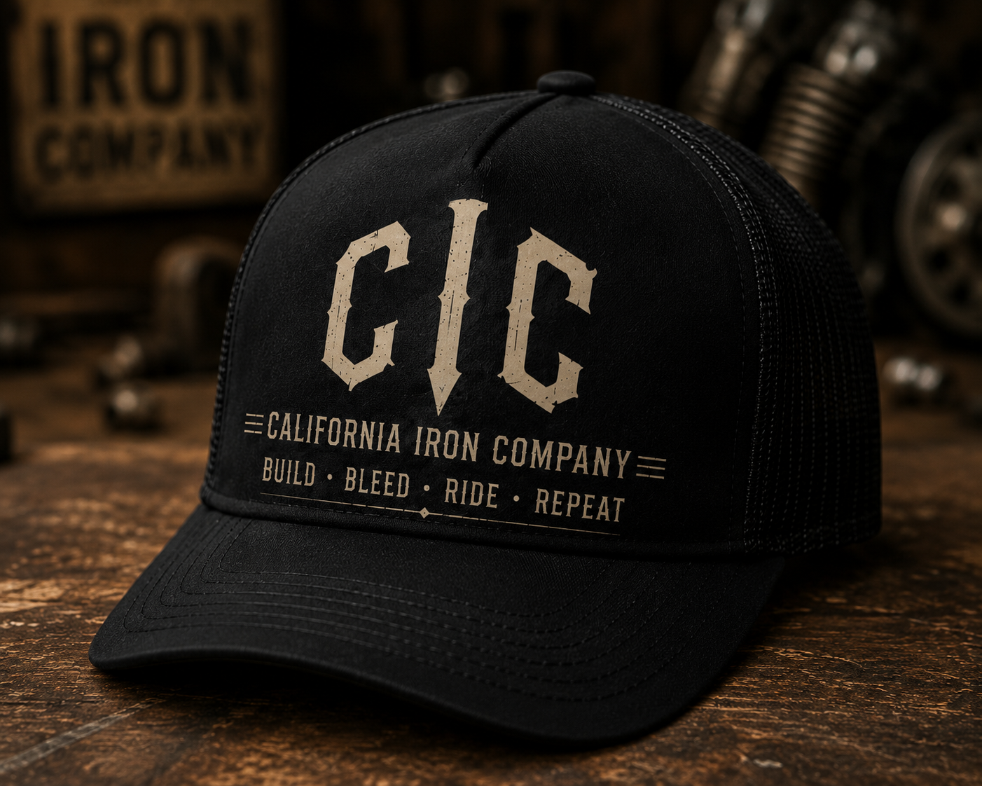 Black trucker hat with California Iron Company logo and slogan, on a wooden surface with gym equipment in background.