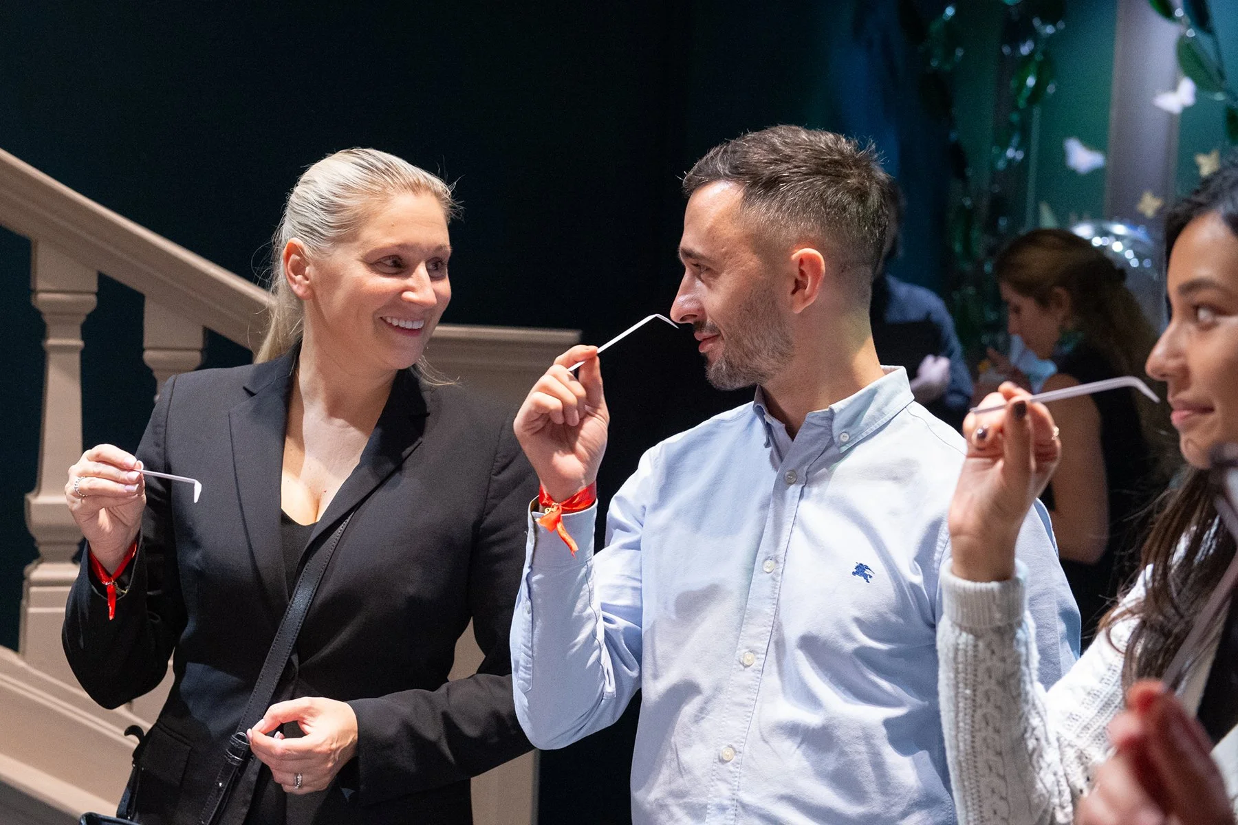 Smiling woman in black blazer talking to a man in white shirt at social gathering.