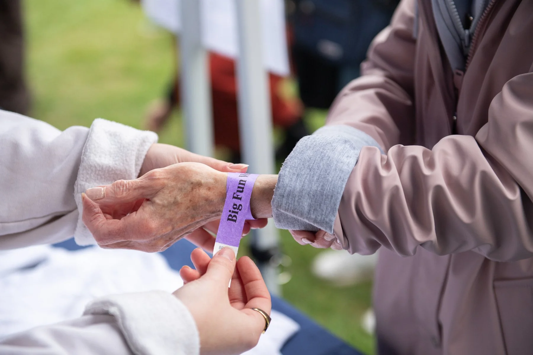 A person receiving a wristband that reads 'Big Fun' at an outdoor event, with another hand helping to put it on.