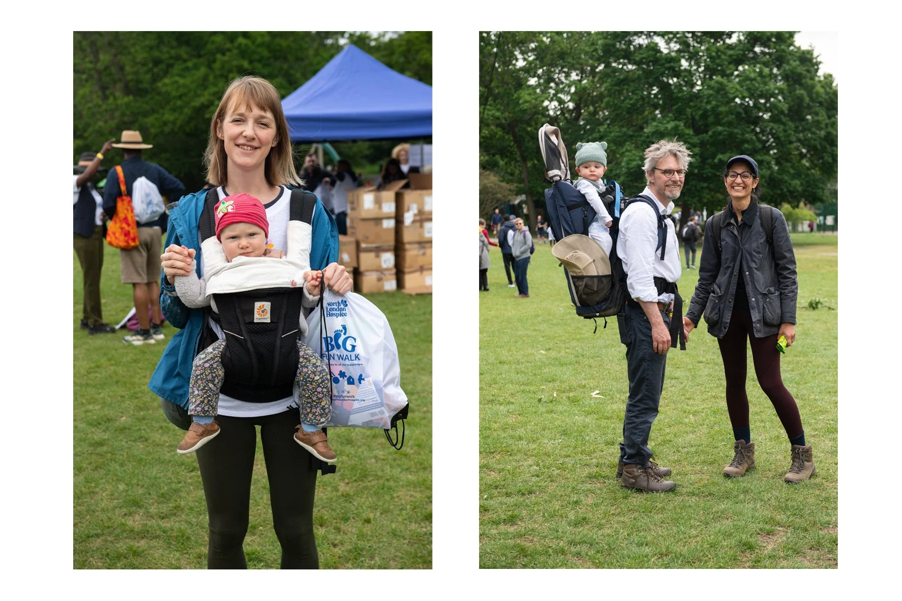 A woman smiling as she carries a young girl in a baby carrier during an outdoor event, with people, boxes, and a blue tent in the background, on a grass field surrounded by trees.