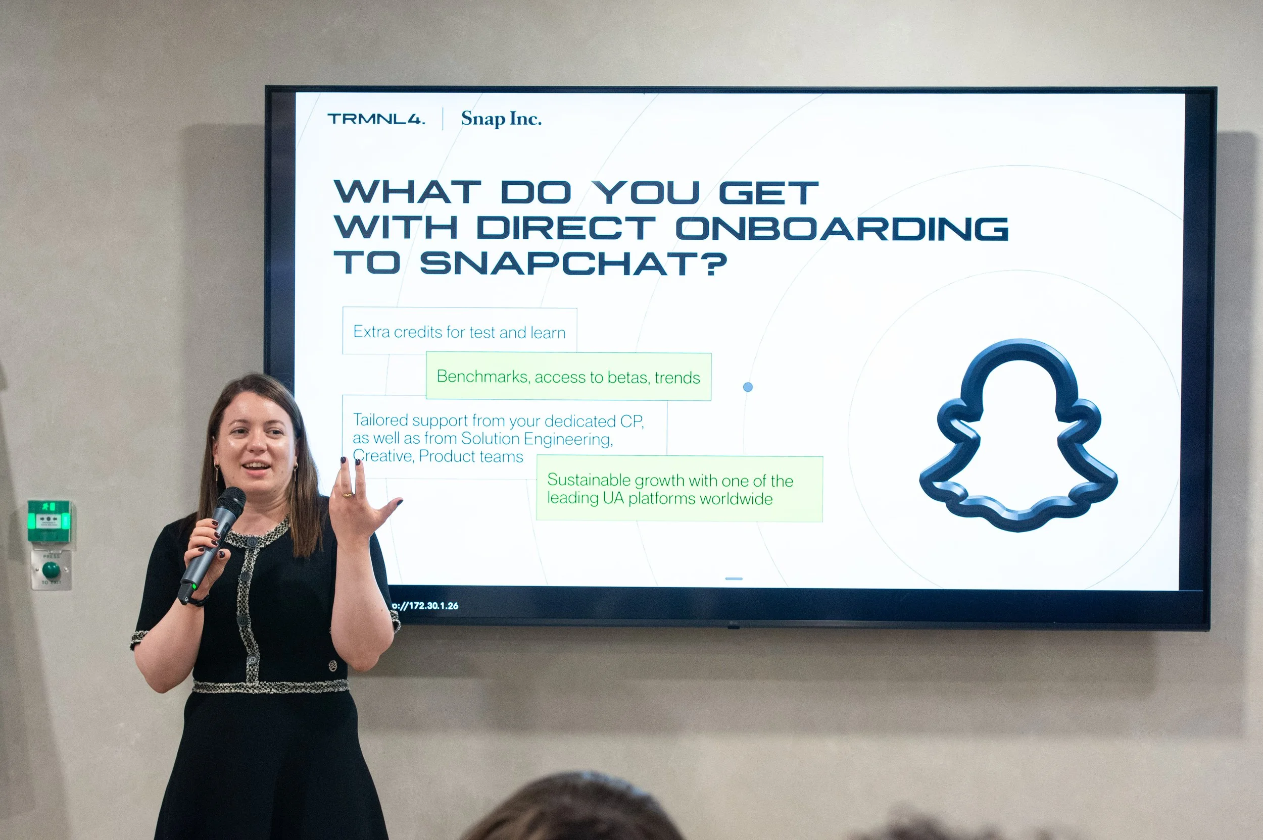 A woman holding a microphone and gesturing with her right hand, standing in front of a large presentation screen displaying a slide about direct onboarding to Snapchat, with a stylized icon of a bunny's head on the right side of the slide.