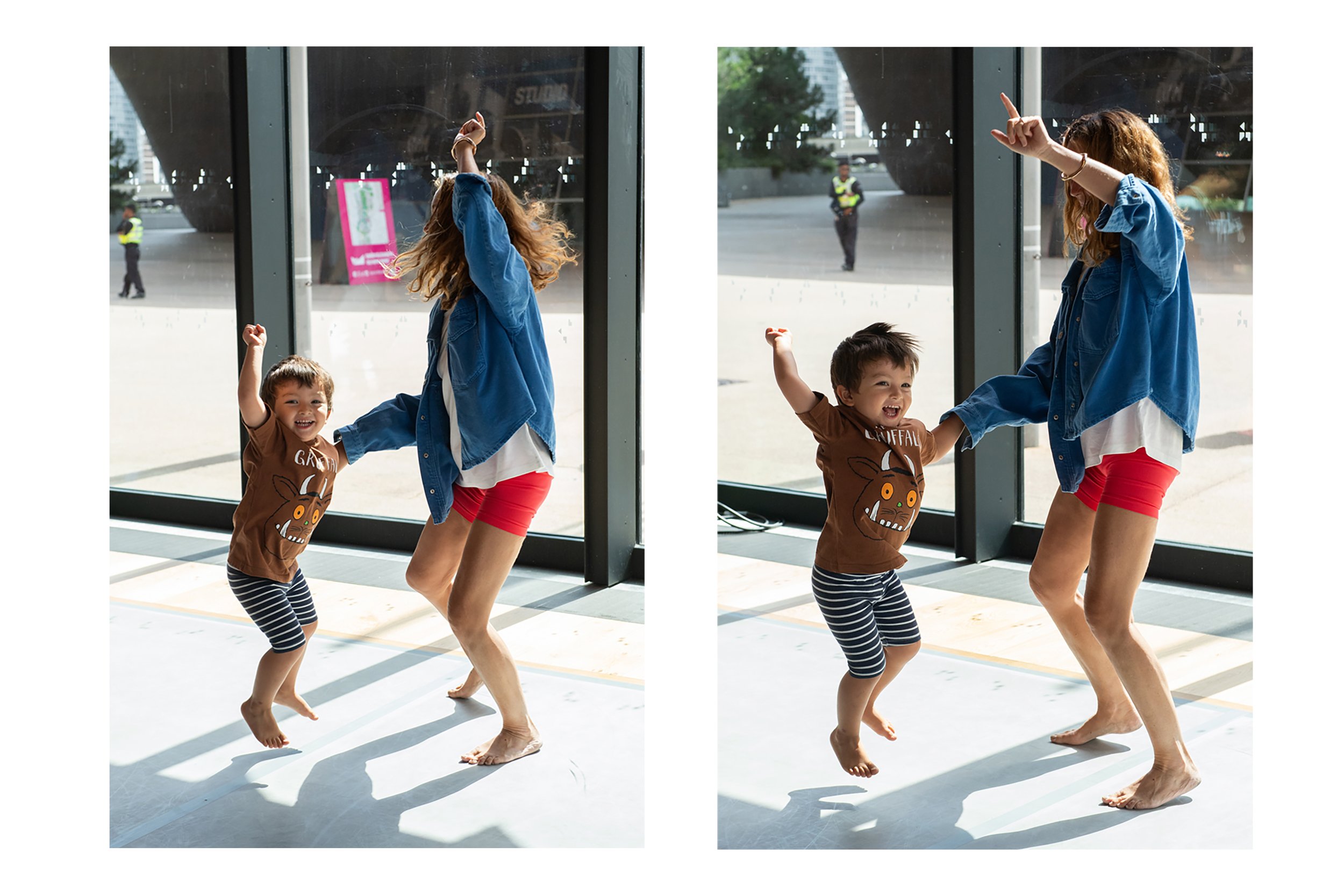 A young girl and woman dancing barefoot inside a building near a glass window. The girl is wearing a brown T-shirt with a deer face and striped leggings, while the woman is wearing red shorts and a blue denim jacket. Outside the window, security pers