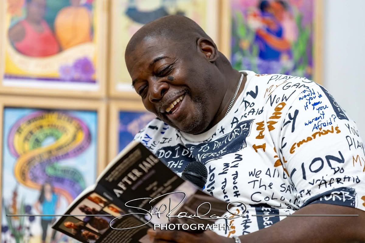 Man smiling while reading a book in front of colorful artwork at an art gallery.