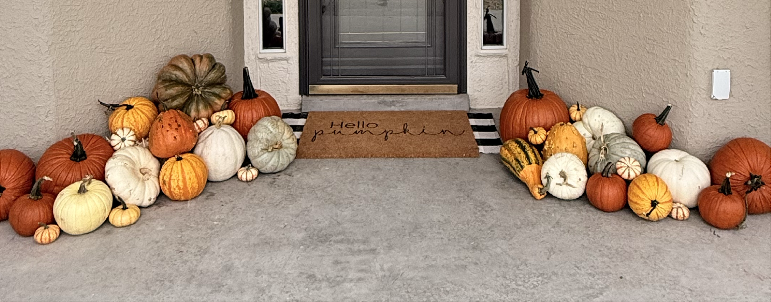 Fall pumpkins and gourds arranged on porch steps with a welcome mat that reads 'Hello pumpkin' in front of a door.