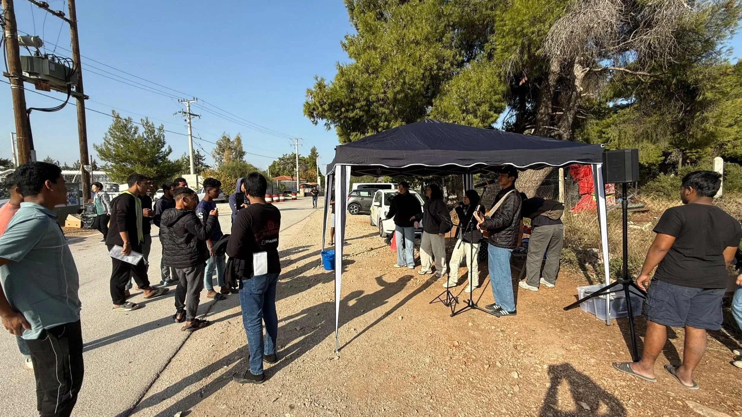 Young adults gathering for outdoor worship and fellowship near a refugee camp in Greece.