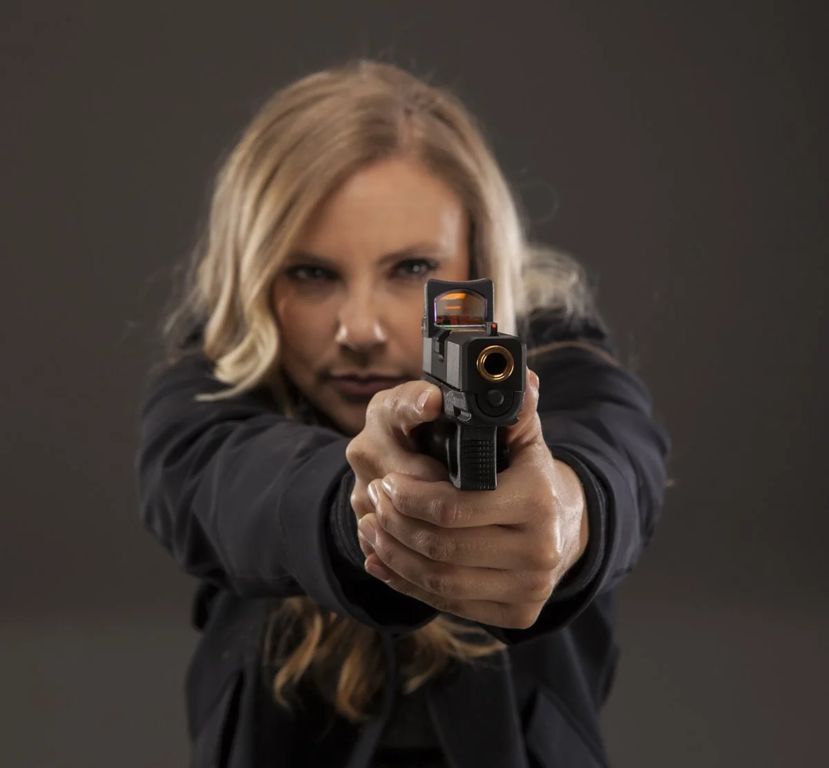 Woman with blonde hair aiming a handgun directly at the camera