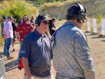 People at an outdoor shooting range, some wearing ear protection and shooting targets in the background.