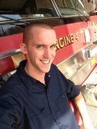 A smiling young man taking a selfie in front of a fire truck.
