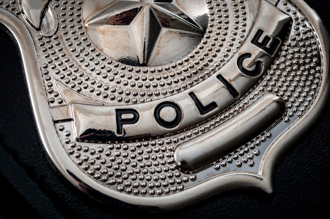 Close-up of a metallic police badge with a star in the center, decorative patterns, and the word 'POLICE' engraved on it.