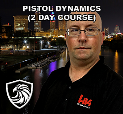 A man wearing glasses and a black polo shirt with a logo, standing in front of a nighttime cityscape with illuminated buildings and a river. Text on the image reads "Pistol Dynamics (2 Day Course)."