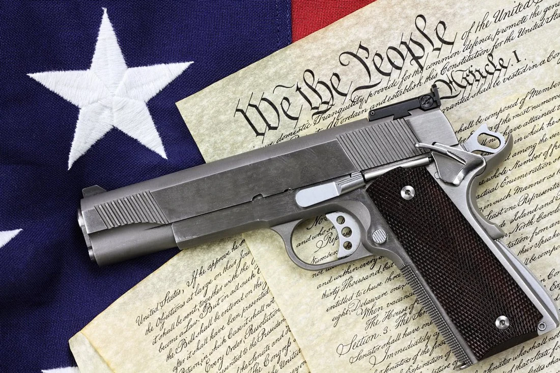 A silver handgun with a black grip resting on the United States Constitution, placed on an American flag background.
