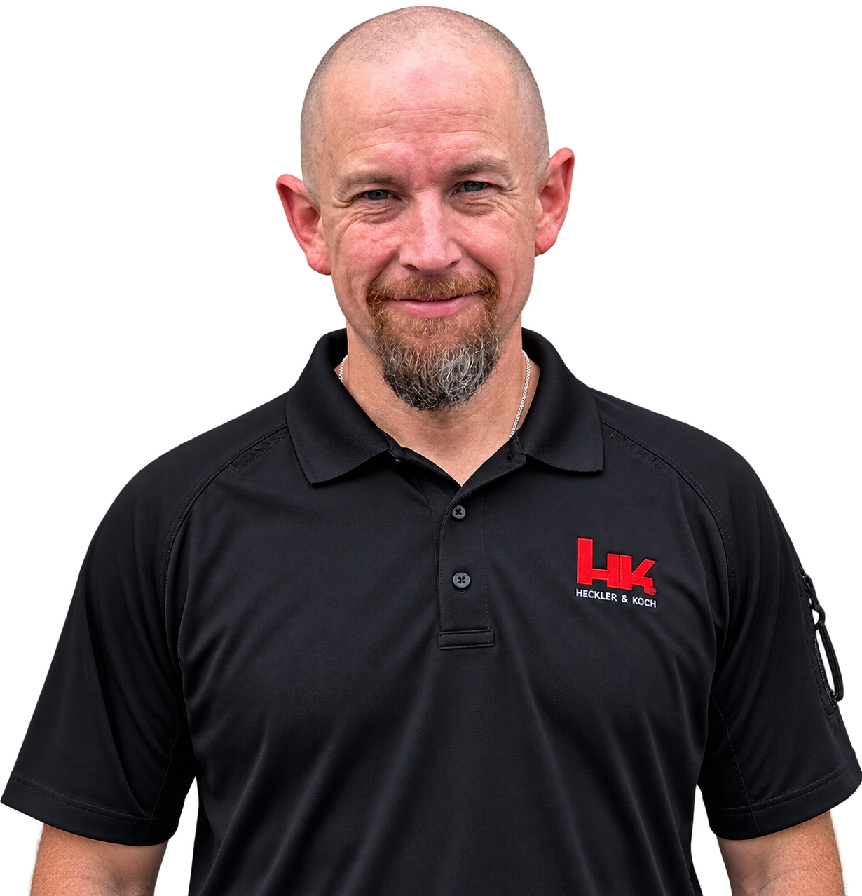 A smiling man with a shaved head and goatee wearing a black polo shirt with the Heckler & Koch logo.