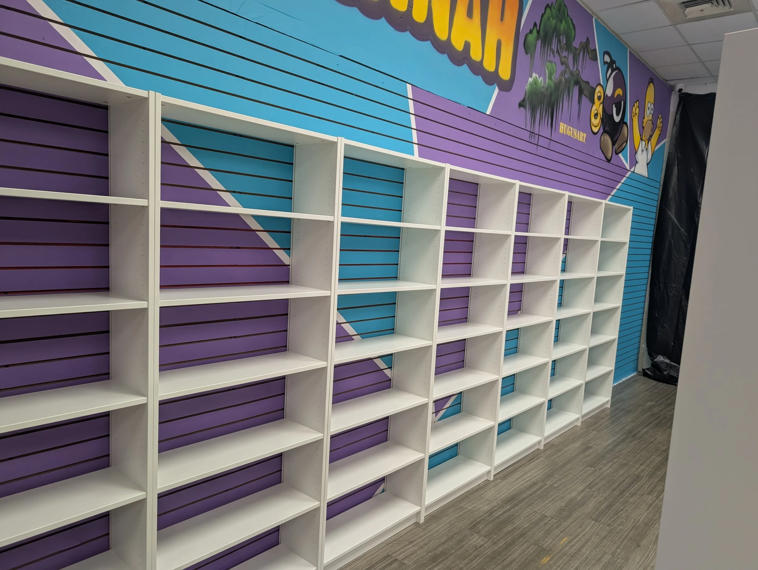 Empty white shelves against a colorful purple and blue wall with cartoon characters and artwork.