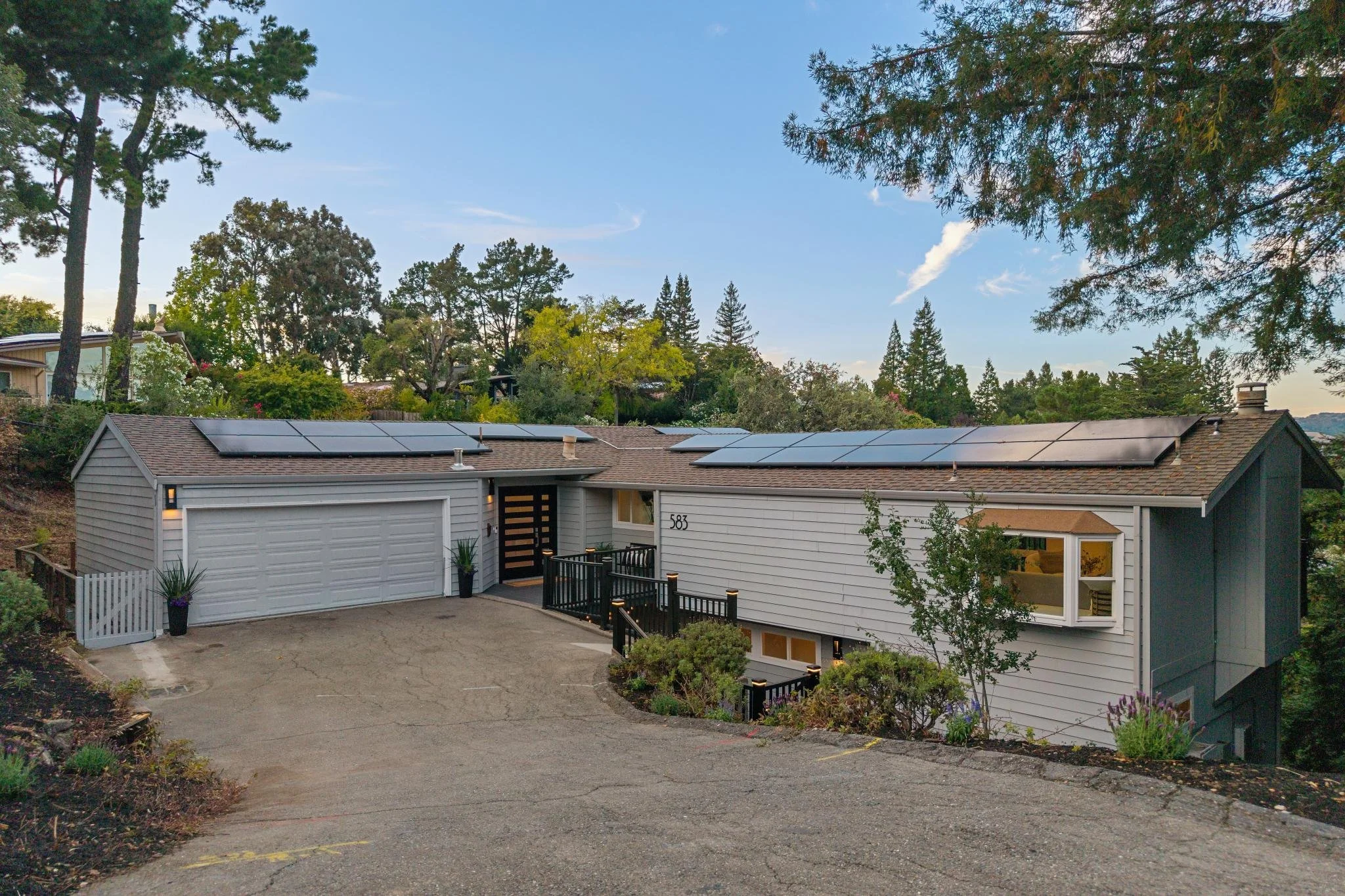 A residential house with solar panels installed on the roof, surrounded by trees and a clear blue sky.