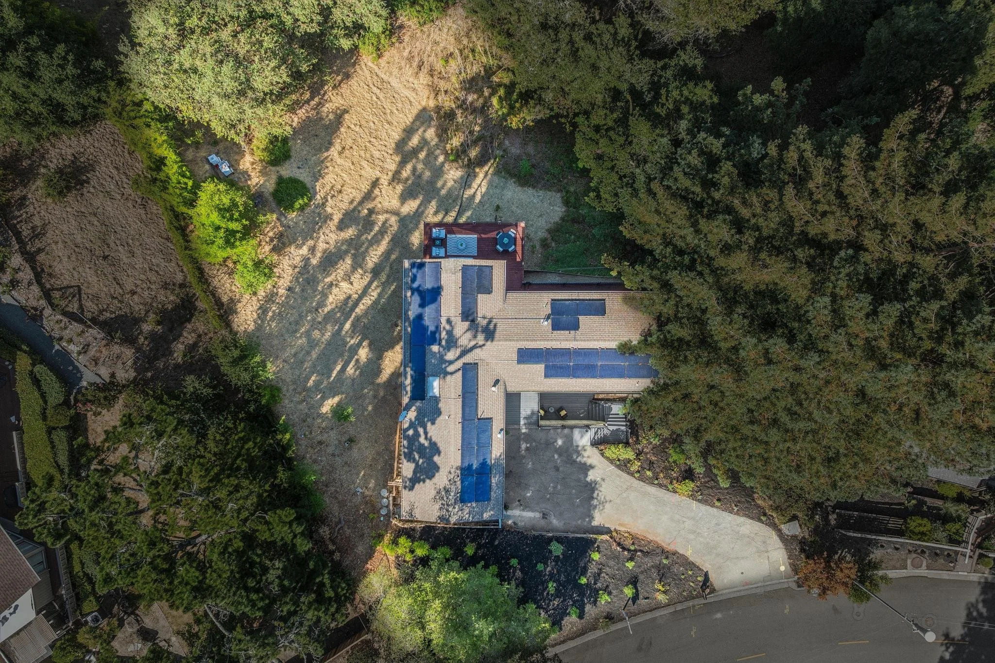 An aerial view of a house with solar panels on the roof surrounded by trees and greenery.