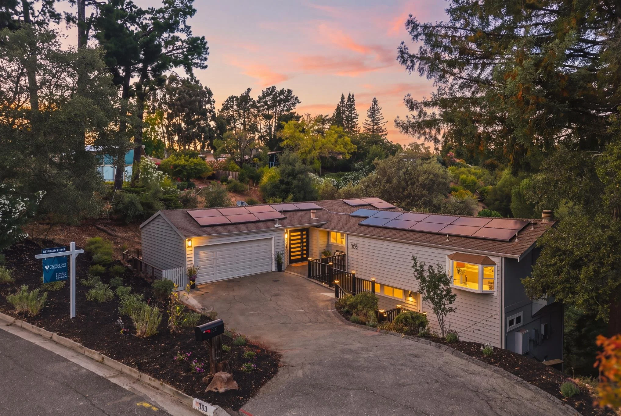 A house with solar panels on the roof, illuminated by outdoor lights, surrounded by trees and a garden, at sunset.