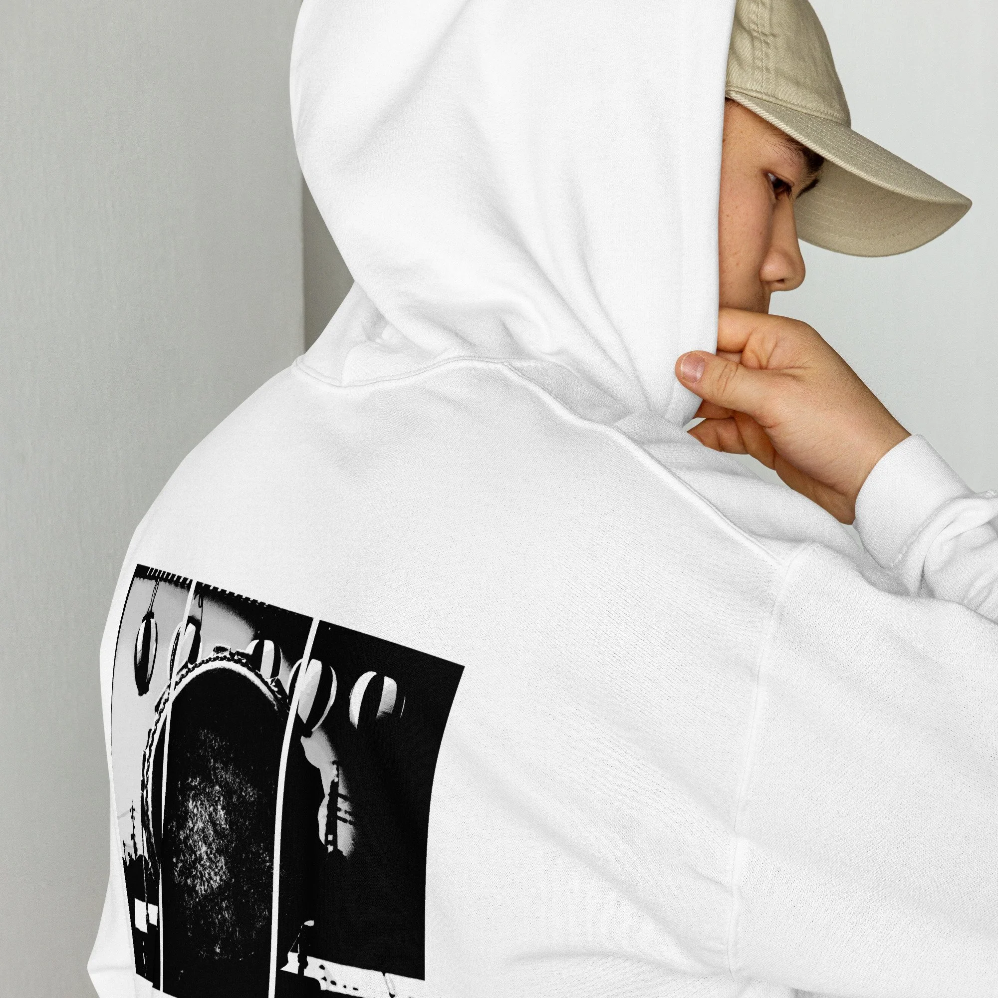 A person wearing a beige baseball cap and white hoodie, holding a black and white printed poster.