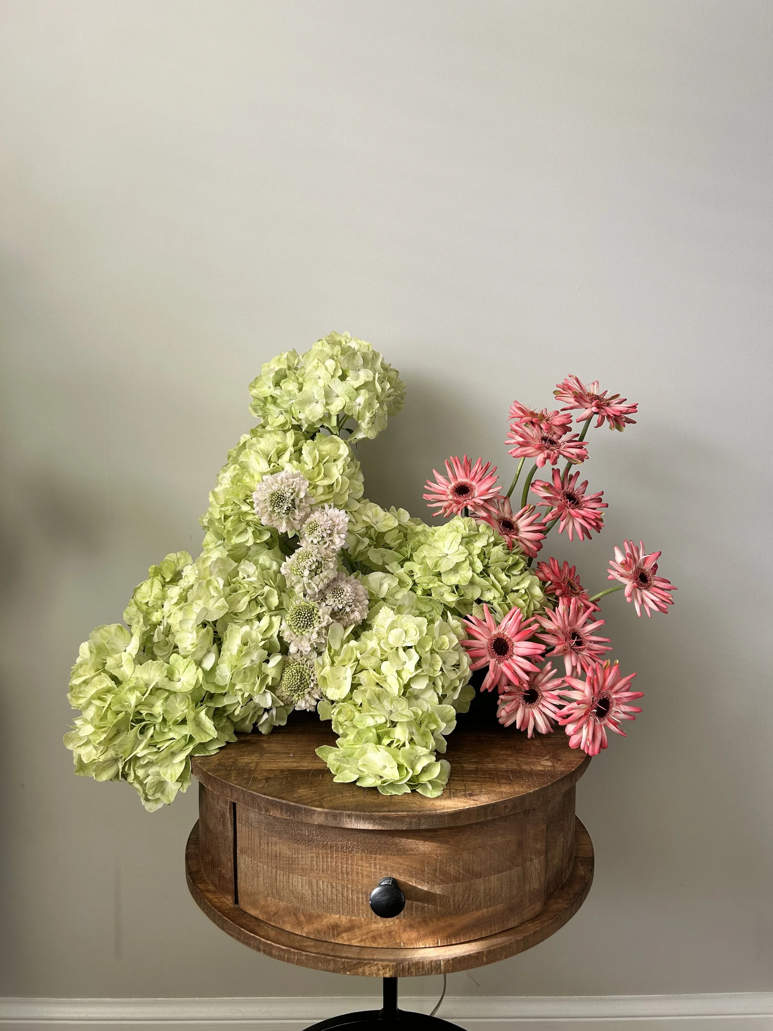 Arrangement of white and pink flowers on a wooden table against a plain wall.