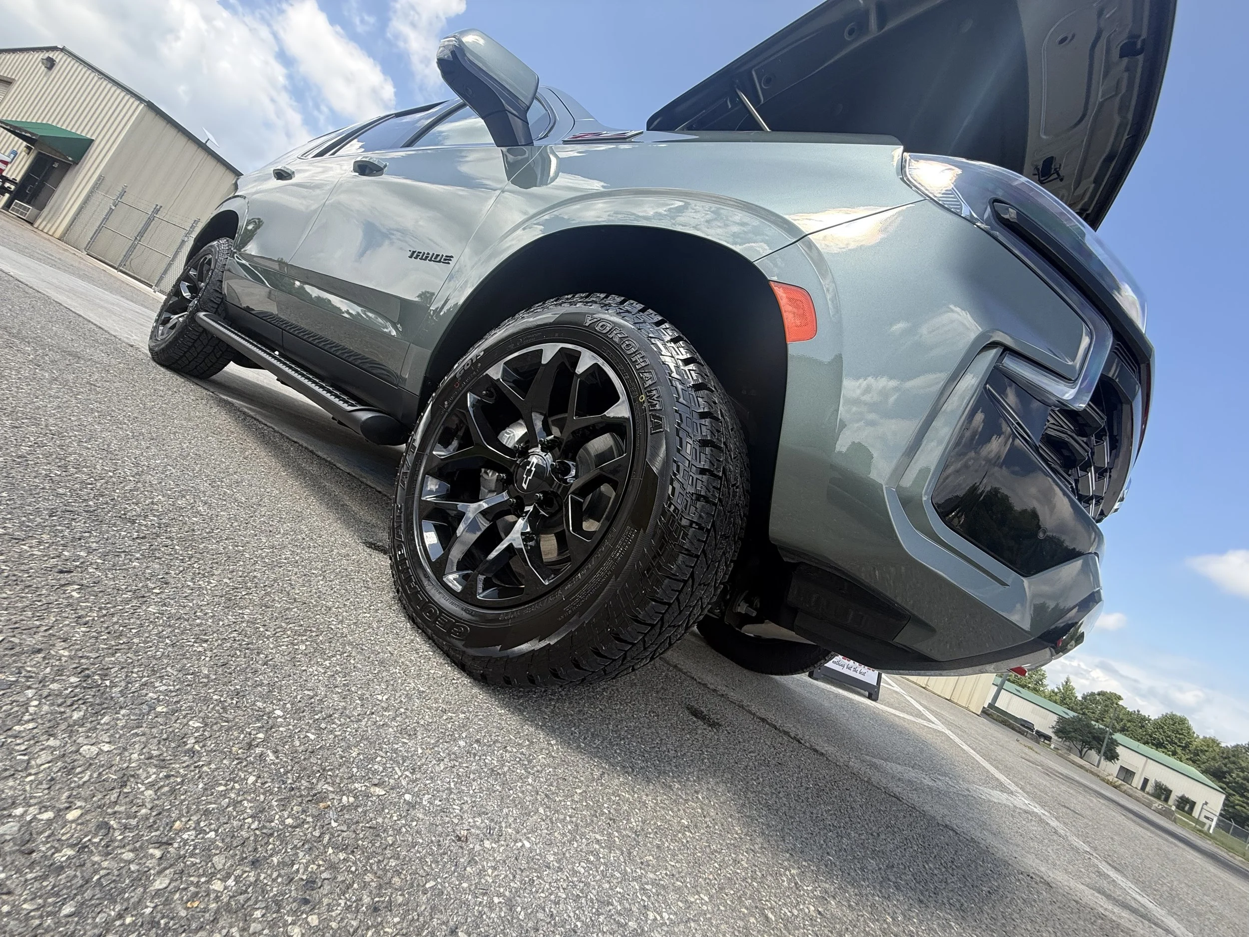 A silver Chevrolet SUV with the hood open, parked on a gravel lot under a partly cloudy sky.