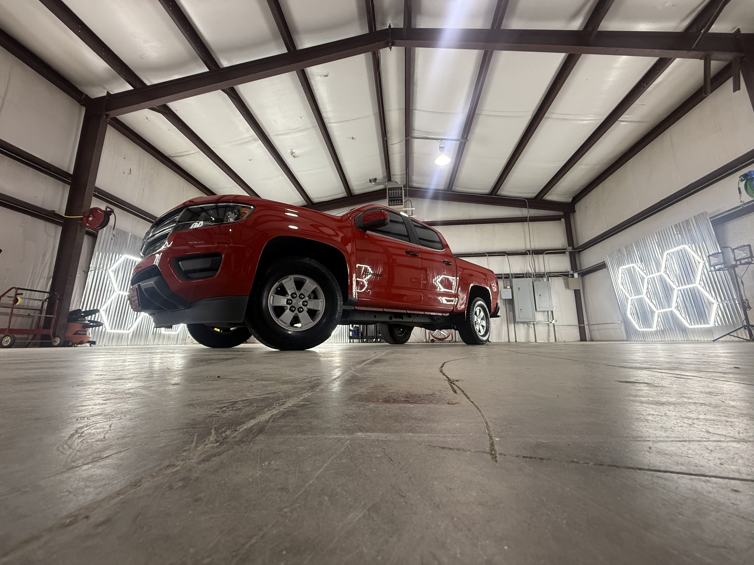 A red pickup truck parked inside a warehouse with high ceiling, exposed metal beams, bright lighting, and concrete floor.