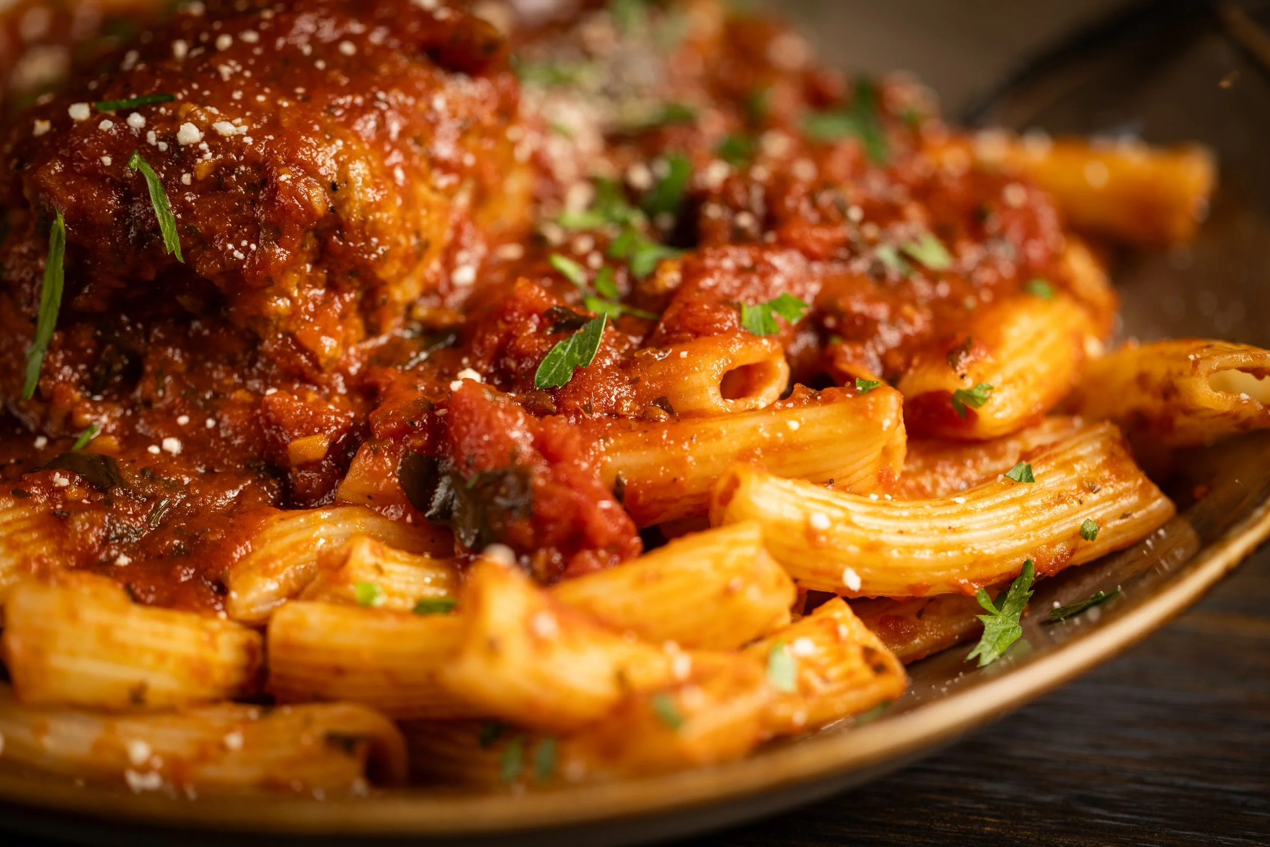 Close-up of spaghetti pasta with marinara sauce, garnished with chopped parsley and grated cheese.