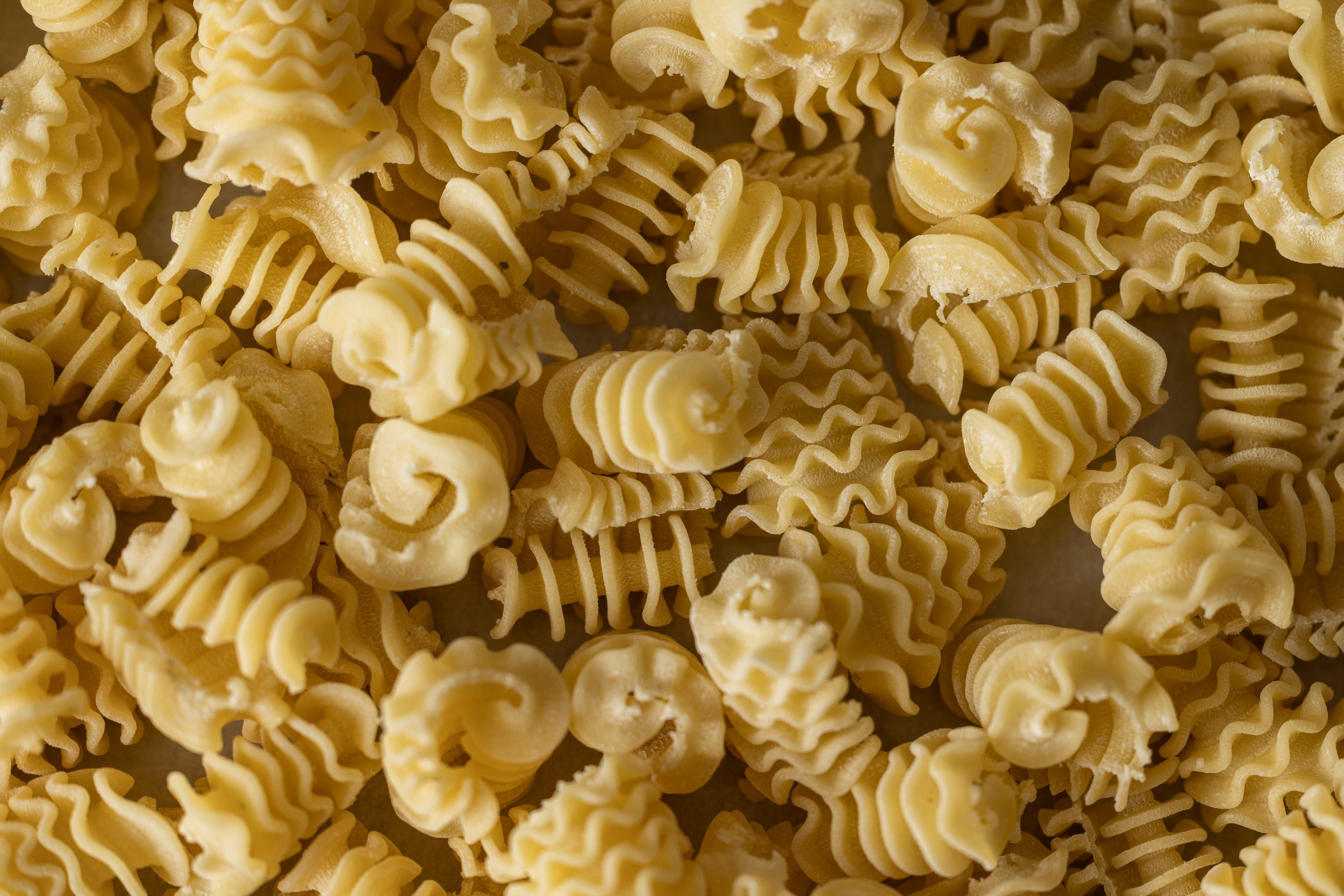 Close-up of uncooked yellow pasta with curly, wavy, and ridged shapes.