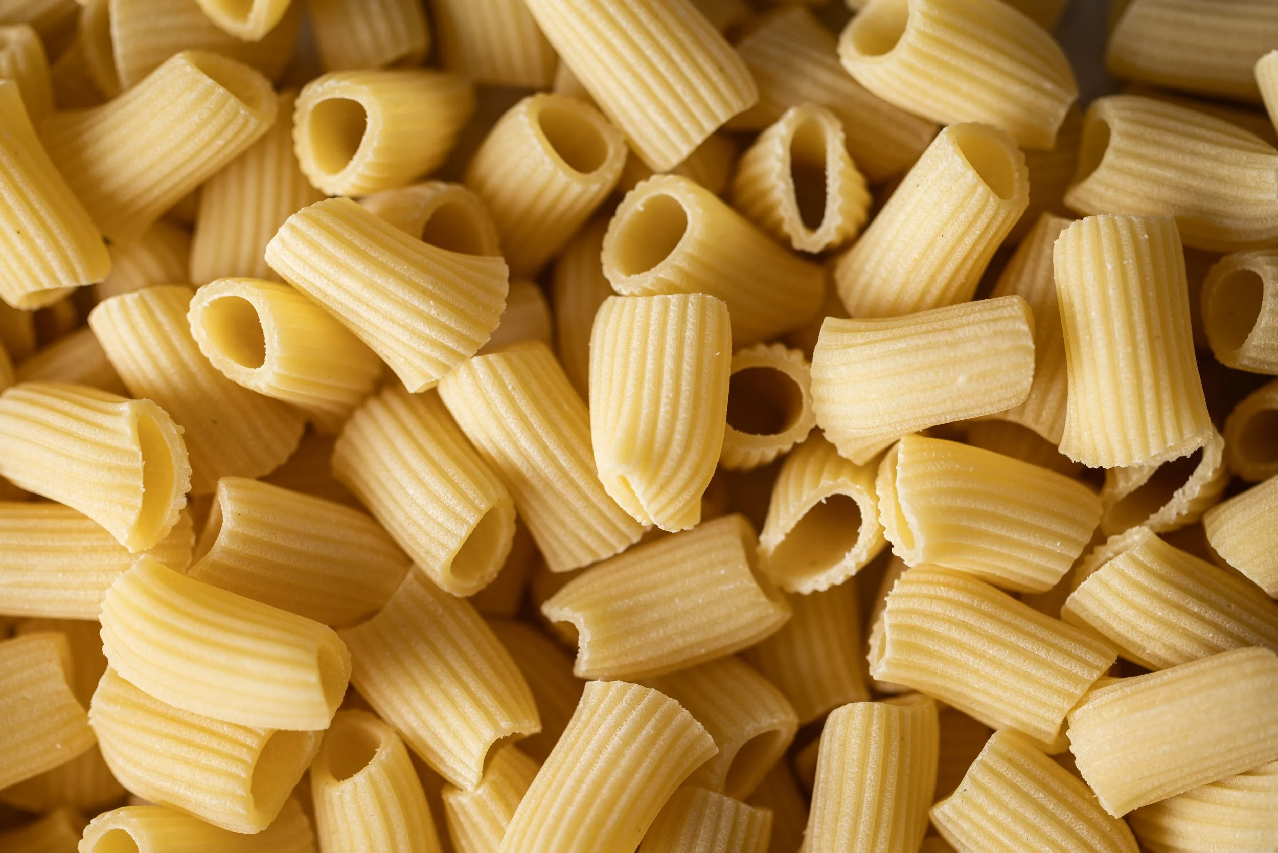 Close-up of uncooked rigatoni pasta with ridged surface and hollow centers.