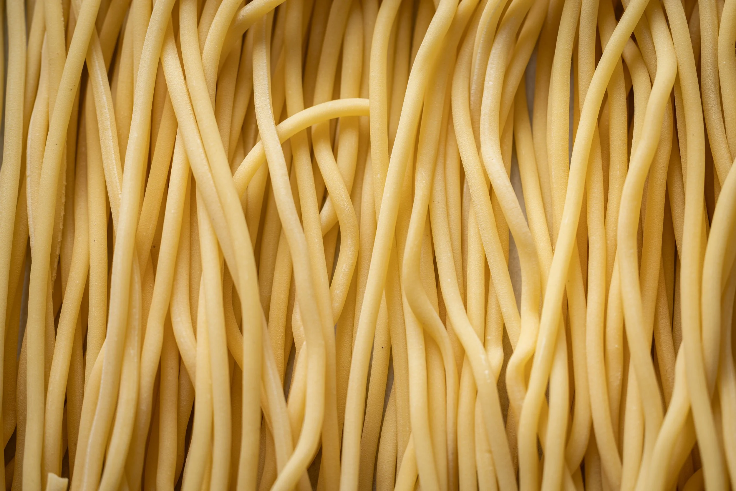 A close-up of uncooked yellow spaghetti noodles piled together.