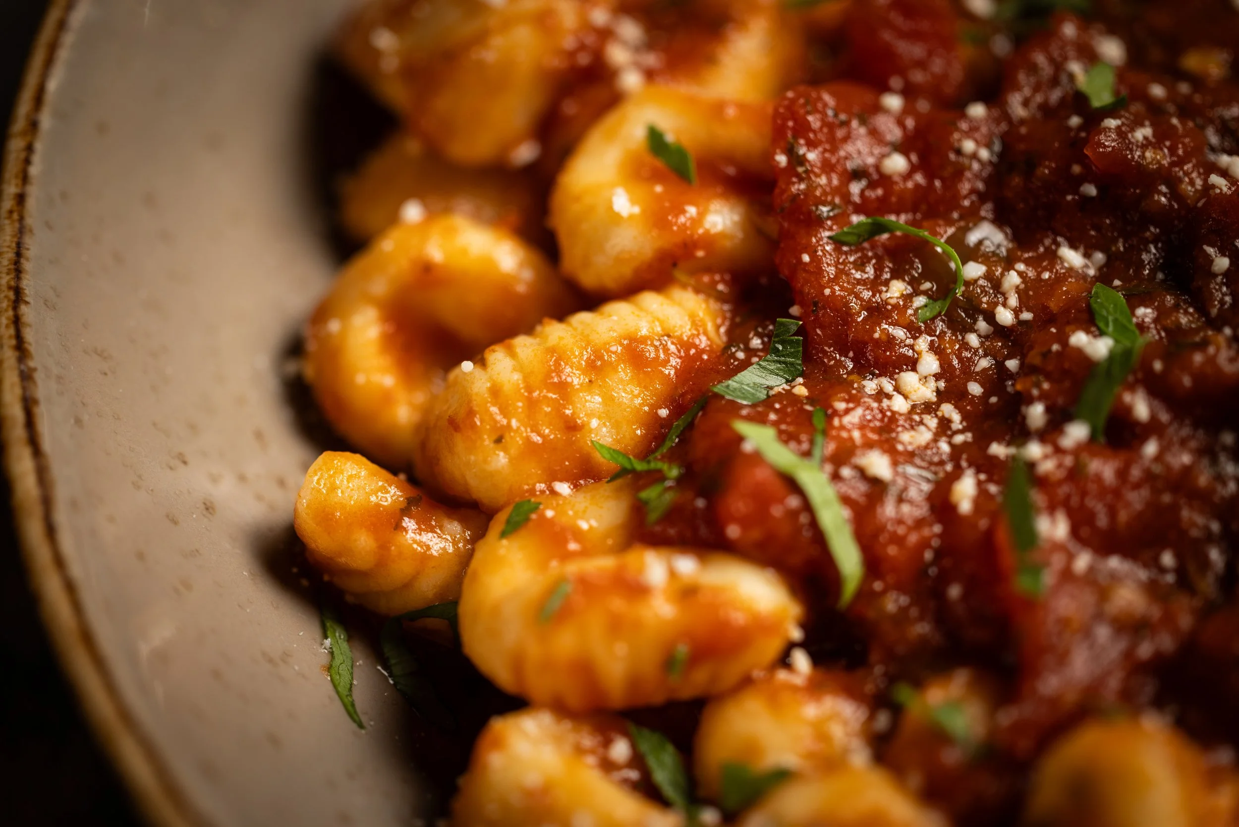 Close-up of gnocchi with tomato sauce, garnished with chopped herbs and grated cheese in a bowl.